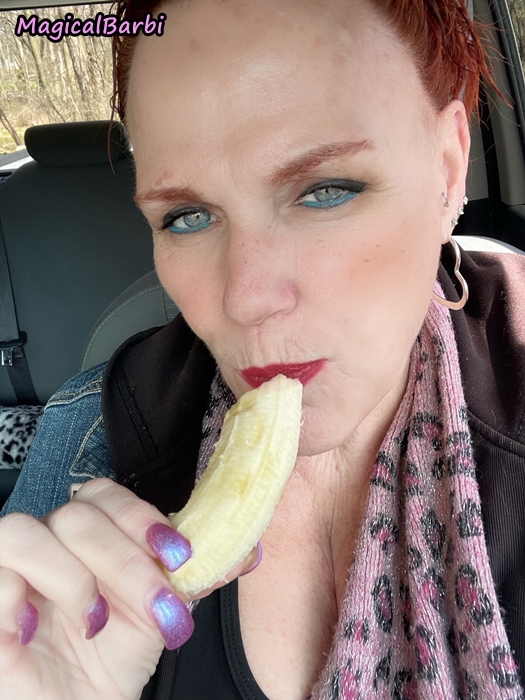 Beautiful redhead is holding a banana to her red painted lips with an intense look in her blue eyes.